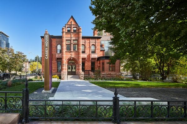Ornate red brick Casey House building with green lawn, pathway, and a clear blue sky.