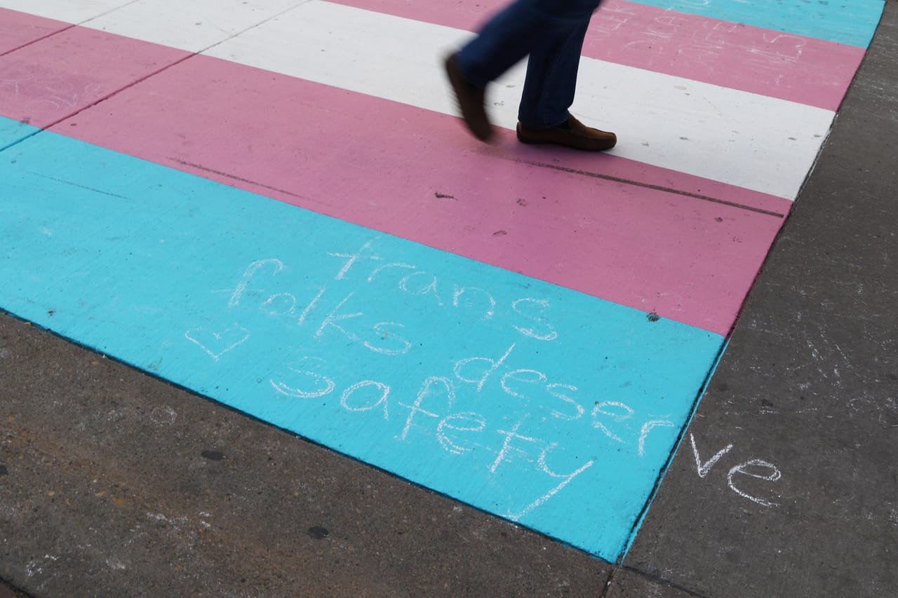 Transgender flag colors on a crosswalk with chalk message: 'trans folks deserve safety'.
