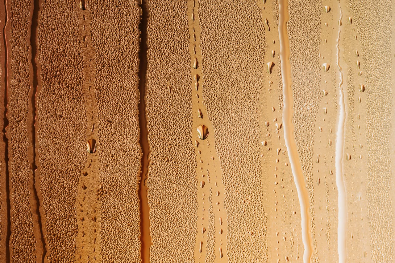 Condensation on a warm-toned glass surface with prominent water streaks and droplets.